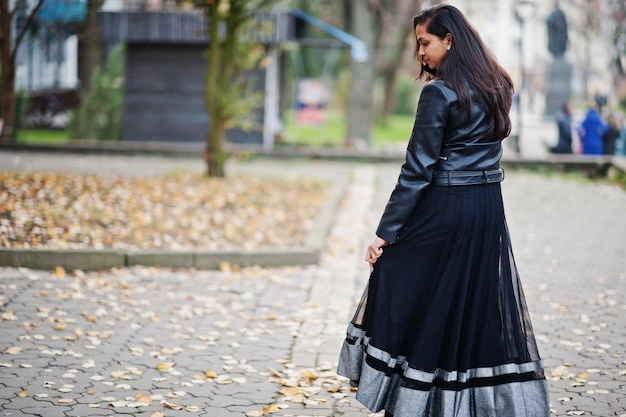Bonita chica india con vestido de sari negro y chaqueta de cuero posada al aire libre en la calle de otoño