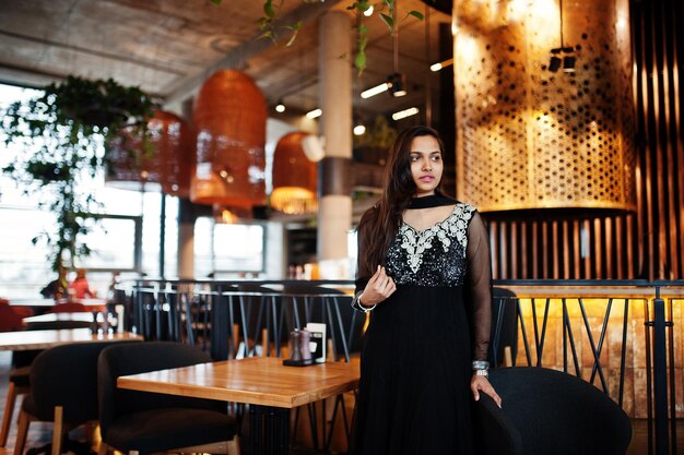 Bonita chica india con vestido de sari negro posado en el restaurante