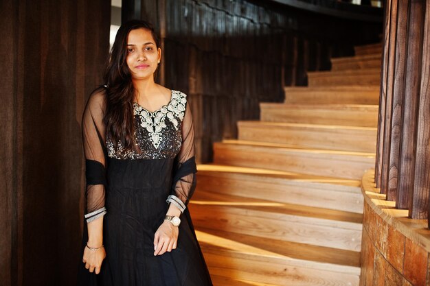 Bonita chica india con vestido de sari negro posado en el restaurante