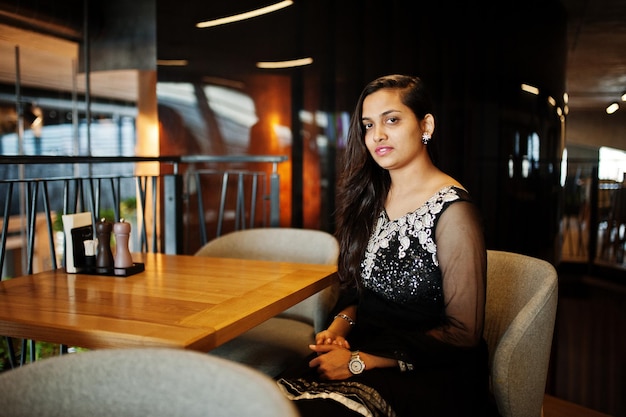 Bonita chica india con vestido de sari negro posado en el restaurante