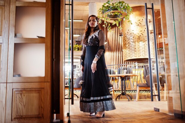 Bonita chica india con vestido de sari negro posado en el restaurante