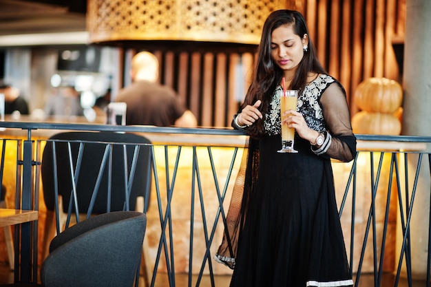 Bonita chica india con vestido de sari negro posó en el restaurante con jugo de naranja a mano