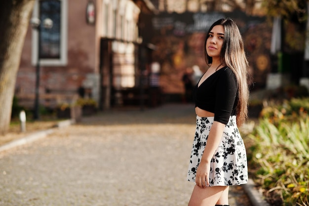 Bonita chica modelo latina de Ecuador vestida con tops negros y falda posada en la calle