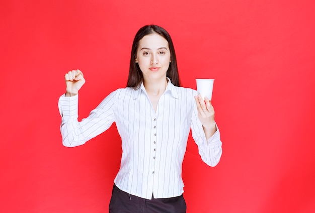 Bonita empresaria posando con una taza de té de plástico sobre fondo rojo.