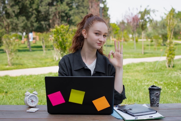 Bonita estudiante independiente que trabaja en una computadora portátil al aire libre que se muestra bien