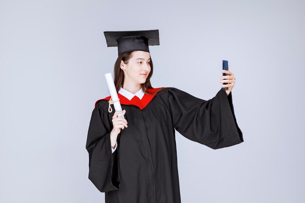Bonita estudiante de posgrado en bata tomando selfie. Foto de alta calidad