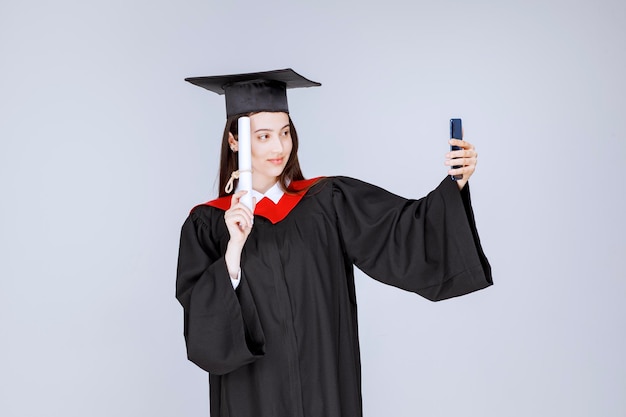 Bonita estudiante de posgrado en bata tomando selfie. Foto de alta calidad