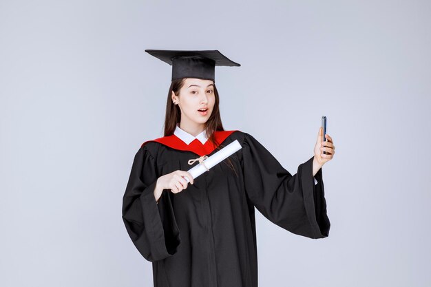 Bonita estudiante de posgrado en bata tomando selfie. Foto de alta calidad