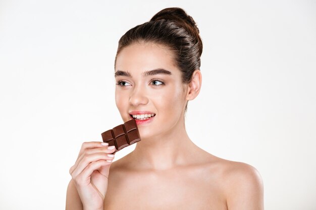 Bonita imagen de una mujer hambrienta semidesnuda con cabello oscuro comiendo una barra de chocolate que no está a dieta