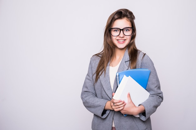 Bonita y joven estudiante con gafas grandes cerca de algunos libros sonriendo sobre fondo blanco.