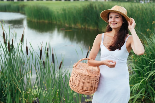 Bonita madre posando junto al lago con cesta de picnic