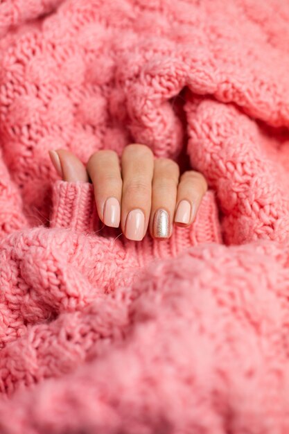 Bonita manicura de color nude, un dedo dorado brillante, sobre fondo de lana rosa tejida.