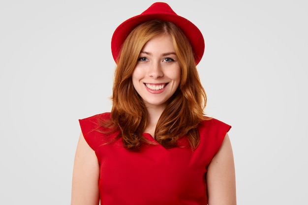 Bonita modelo femenina con sonrisa positiva vestida con elegante sombrero rojo y blusa, va a tener una cita con su novio