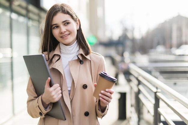 Bonita modelo en ropa casual se queda con su computadora portátil y café al aire libre