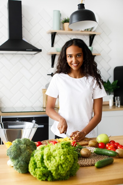 Bonita mujer afro está cortando un pimiento amarillo y sonriendo