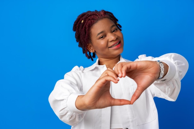 Bonita mujer afro puso las manos en forma de corazón contra el fondo azul.