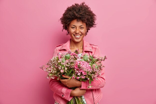 Bonita mujer afroamericana expresa emociones sinceras, abraza un ramo de flores, tiene un estado de ánimo primaveral