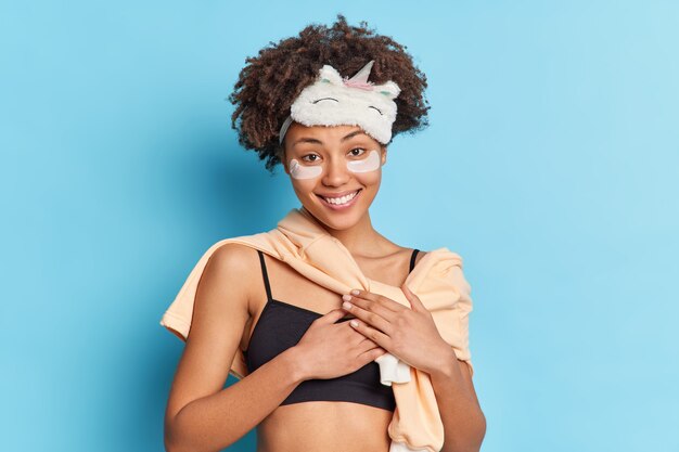 Bonita mujer afroamericana sonríe aplica suavemente parches de colágeno debajo de los ojos para refrescar la piel