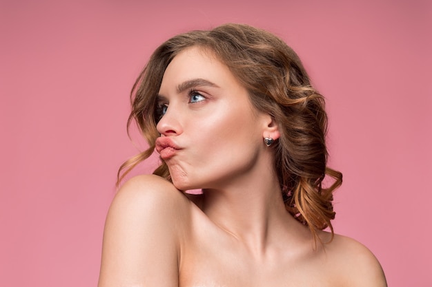 Bonita mujer joven con cabello largo y sedoso ondulado, maquillaje natural con la mano cerca de la barbilla aislada en la pared rosa. Modelo con maquillaje natural.