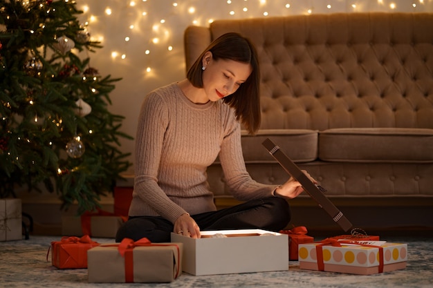 Bonita mujer morena abre un adorable regalo sosteniendo un globo de Navidad blanco