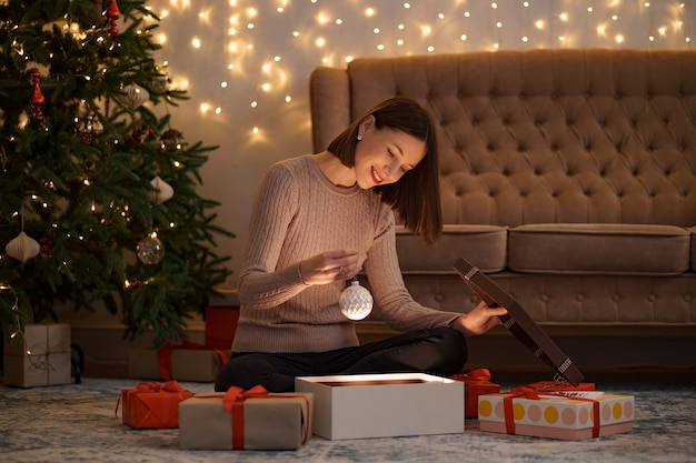 Bonita mujer morena abre un adorable regalo sosteniendo un globo de Navidad blanco