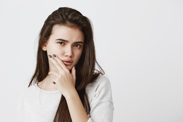 Bonita mujer morena con ojos oscuros con el pelo suelto frunciendo el ceño. Pensativa joven con expresión perpleja pensando en algo