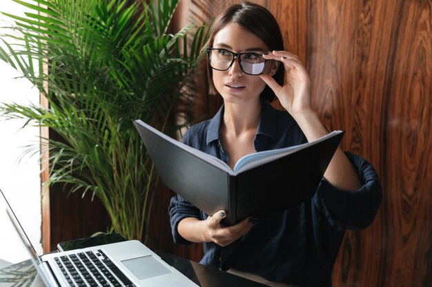 Bonita mujer de negocios en anteojos sentado junto a la mesa