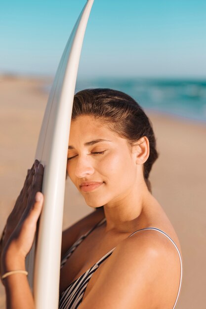 Bonita mujer con ojos cerrados y tabla de surf.