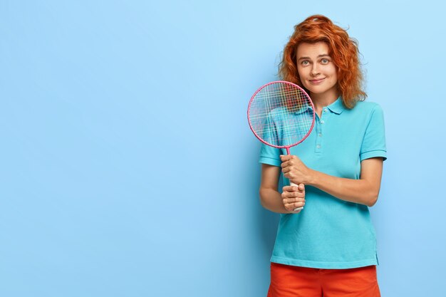 Bonita mujer pelirroja con cabello rizado, le gusta el tenis, sostiene la raqueta, lista para jugar, viste ropa casual de verano
