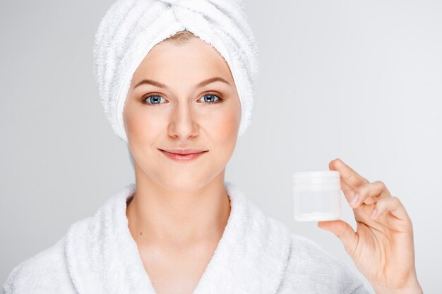 Bonita mujer rubia con una toalla de baño sobre el cabello mostrando crema