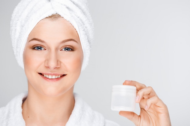 Bonita mujer rubia con una toalla de baño sobre el cabello mostrando crema