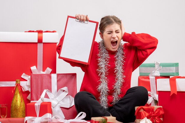 Bonita mujer sentada alrededor de regalos de Navidad con nota sobre blanco