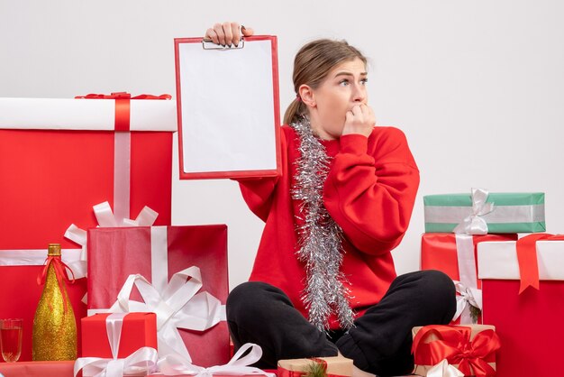 Bonita mujer sentada alrededor de regalos de Navidad con nota sobre blanco