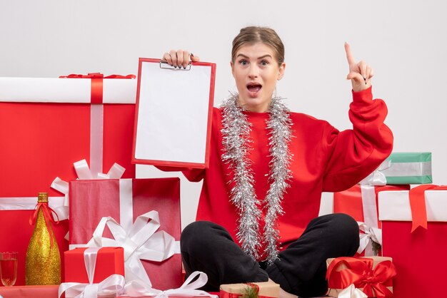 Bonita mujer sentada alrededor de regalos de Navidad con nota sobre blanco