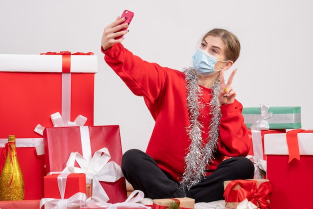 Bonita mujer sentada alrededor de los regalos de Navidad tomando selfie en blanco