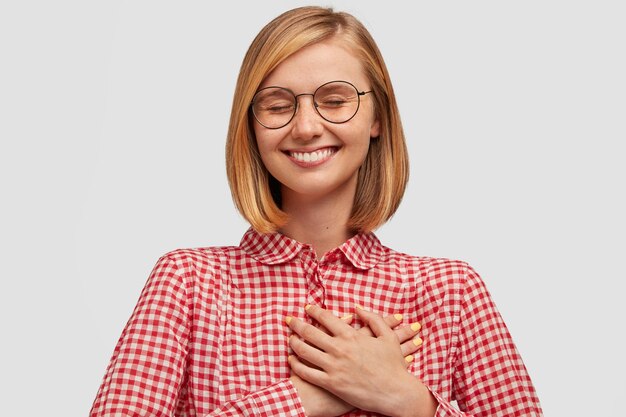 Bonita mujer sonriente con una sonrisa encantadora, mantiene los ojos cerrados y toca el corazón