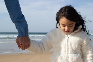 Foto gratis bonita niña japonesa sosteniendo la mano de los padres. hija de cabello oscuro caminando en la playa con papá. familia, concepto de vacaciones