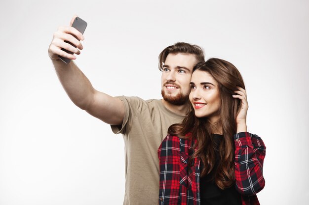 Bonita pareja alegre tomando selfie en teléfono, mirando feliz.