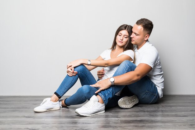 Bonita pareja elegante abrazándose juntos mientras está sentado en el suelo aislado sobre fondo blanco.