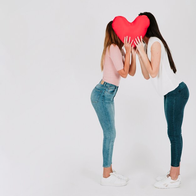 Bonita pareja de lesbianas besándose detrás de corazón