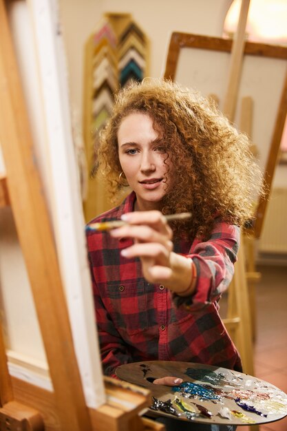 Bonita pelirroja artista rizada con sonrisa dibuja una pintura