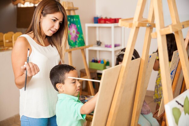 Bonita profesora de arte hispano revisando y calificando el trabajo de un niño pequeño durante la clase