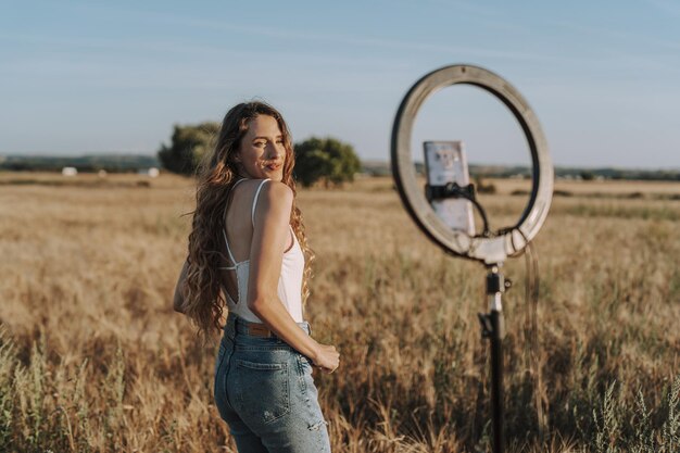 Foto gratuita una bonita rubia española tomando una selfie en un campo con su teléfono montado en una luz de anillo