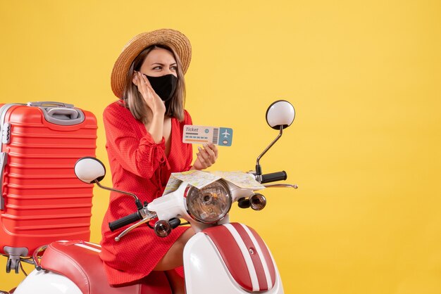 Bonita señorita en ciclomotor con maleta roja sosteniendo el boleto