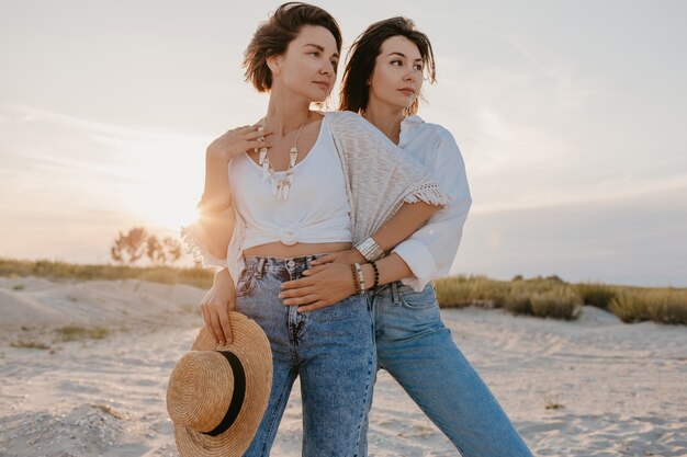 Bonitas dos mujeres jóvenes divirtiéndose en la playa al atardecer, romance de amor lesbiano gay