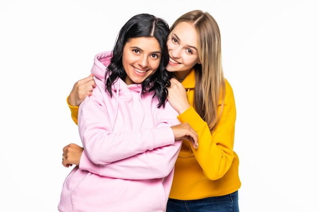 Bonitas dos mujeres vestidas con sudaderas con capucha casuales y jeans aislados pared blanca