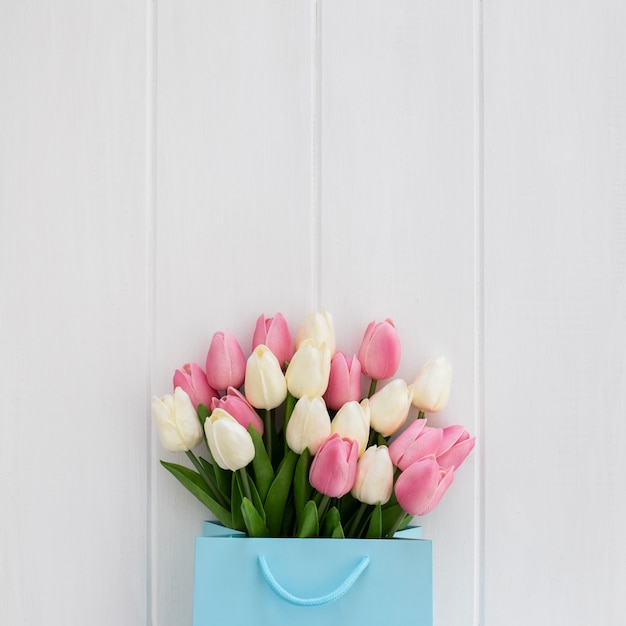 Bonito ramo de tulipanes dentro de una bolsa azul sobre un fondo de madera blanco