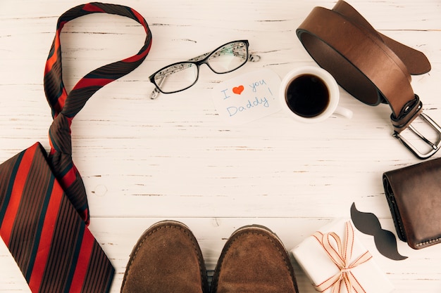 Botas entre accesorios masculinos cerca de regalo y copa de bebida.