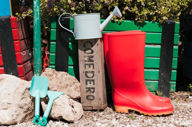 Botas de agua rojas; regadera; herramientas de jardineria en el jardin