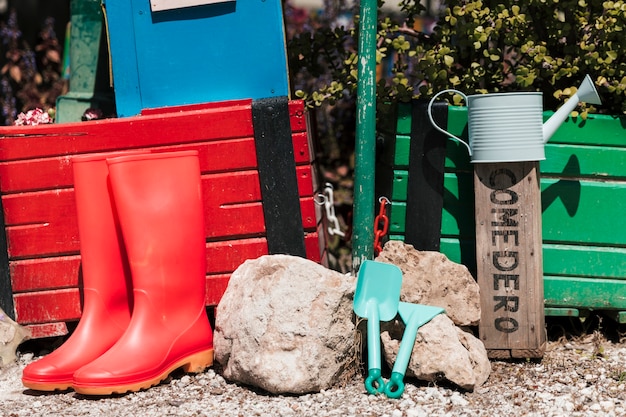 Botas de agua rojas; regadera; herramientas de jardineria en el jardin